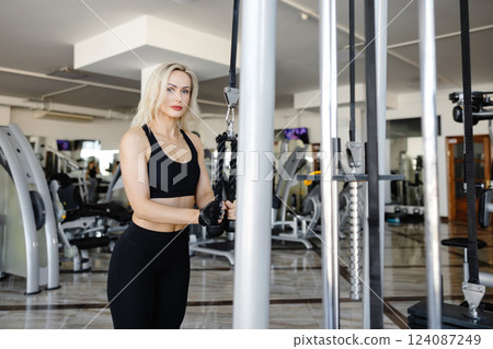 Determined sportswoman exercising back muscles using cable machine in gym 124087249