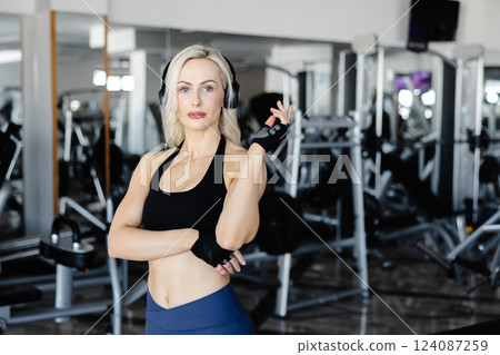 Athletic woman wearing headphones and gloves listening to music at the gym 124087259
