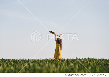 Yellow colored toy plane and clothes. Happy girl have a walk outdoors on the field at summer 124087447