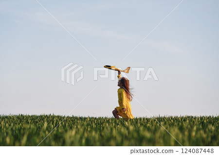 Yellow colored toy plane and clothes. Happy girl have a walk outdoors on the field at summer 124087448