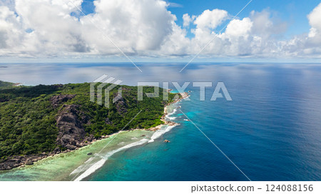 Green hills covered meet the rocky shoreline with waves breaking on the coast. La Digue, Seychelles. Green hills covered meet the rocky shoreline with waves breaking on the coast. La Digue, Seychelles. 124088156