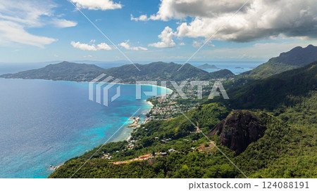 A turquoise bay along a coastal town surrounded by lush green hills under a partly cloudy sky. Seychelles, Mahe. A turquoise bay along a coastal town surrounded by lush green hills under a partly cloudy sky. Seychelles, Mahe. 124088191