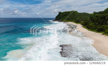 Aerial view of a coastline with clear blue ocean waters and green hills in the background. Anse Bazarca Beach. Seychelles, Mahe. Aerial view of a coastline with clear blue ocean waters and green hills in the background. Anse Bazarca Beach. Seychelles, Mahe. 124088219