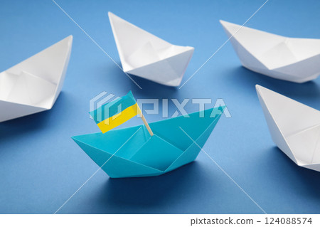 Help for Ukraine concept. White ships and blue paper ship with Ukrainian flag on blue background. Help for Ukraine concept. White ships and blue paper ship with Ukrainian flag on blue background. 124088574