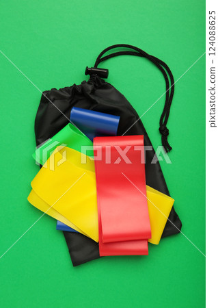 A set of colorful latex rubber bands for fitness and a black cover for them on green background. Sports concept. Vertical photo 124088625