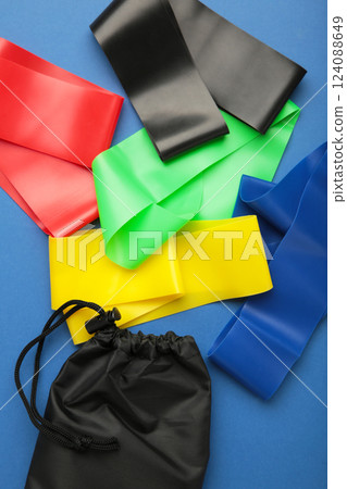 A set of colorful latex rubber bands for fitness and a black cover for them on blue background. Sports concept. Vertical photo 124088649
