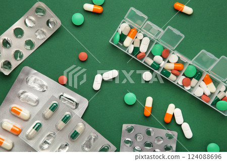 Daily pill box with medications and nutritional supplements on green background. 124088696