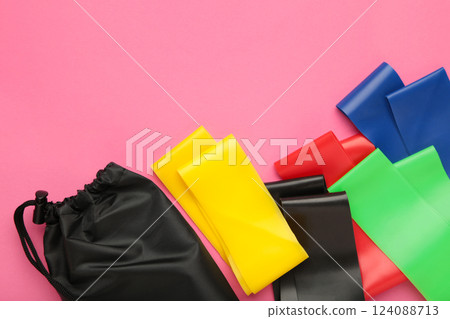 A set of colorful latex rubber bands for fitness and a black cover for them on pink background. Sports concept. Space for text A set of colorful latex rubber bands for fitness and a black cover for them on pink background. Sports concept. Space for text 124088713