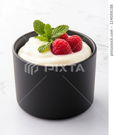 The photo shows yogurt with raspberries and fresh mint leaves, which looks delicious and appetizing on a white background. Juicy berries and creamy yogurt create the perfect balance for dessert. 124089186