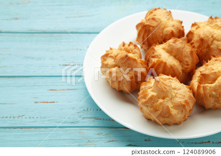 Homemade profiteroles with cream on plate on blue background. Fresh baked golden profiterole. 124089906