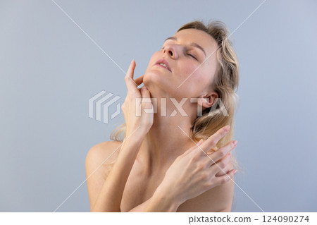 A Serene Portrait of a Young Woman Delicately Touching Her Face in Soft Light Against a Minimalistic Gray Backdrop A Serene Portrait of a Young Woman Delicately Touching Her Face in Soft Light Against a Minimalistic Gray Backdrop 124090274