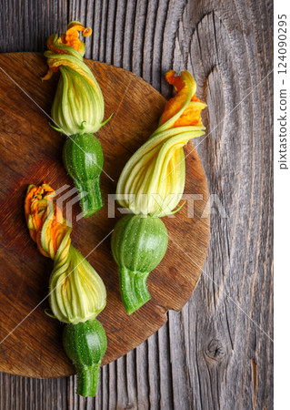 Three young zucchini with flowers on wooden cutting board Three young zucchini with flowers on wooden cutting board 124090295