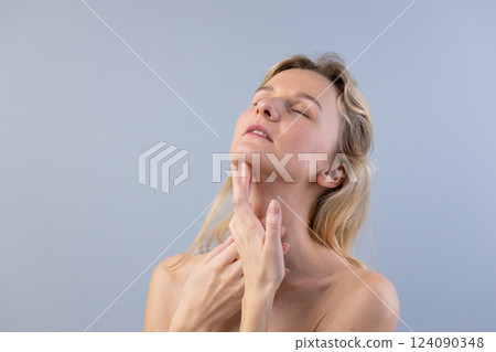 Captivating Portrait of a Young Woman with Soft Expression and Delicate Touching of Her Neck Against a Light Blue Background in a Studio Setting Captivating Portrait of a Young Woman with Soft Expression and Delicate Touching of Her Neck Against a Light Blue Background in a Studio Setting 124090348
