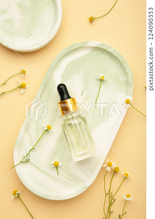 Composition with chamomile flowers and cosmetic bottle of essential oil on plaster tray on beige background Composition with chamomile flowers and cosmetic bottle of essential oil on plaster tray on beige background 124090353