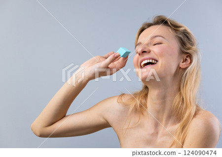 Joyful Woman Laughing While Holding a Small Blue Cube Against Her Face, Demonstrating a Moment of Pure Happiness and Playfulness in a Minimalist Setting 124090474