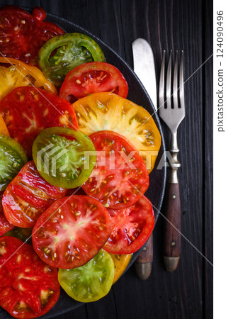 Sliced multi-colored tomatoes on black plate 124090496