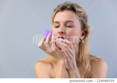 A Woman Applying Makeup with Beauty Blenders as She Focuses on Her Refining Techniques for a Flawless Look in a Minimalistic and Calm Environment A Woman Applying Makeup with Beauty Blenders as She Focuses on Her Refining Techniques for a Flawless Look in a Minimalistic and Calm Environment 124090559