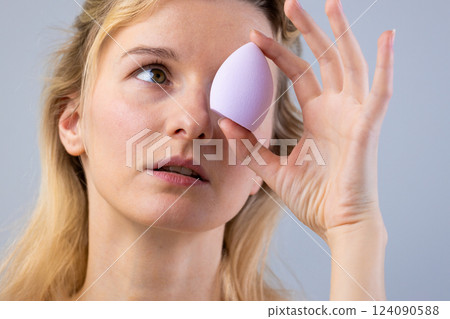 Exploring Makeup Application Techniques: A Close-Up of a Woman Holding a Beauty Blender Near Her Eye for Precision in Cosmetic Application and Enhancing Beauty 124090588
