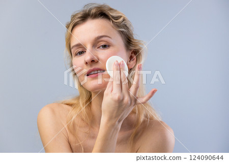 Young Woman Applying Skin Care Product with Cotton Pad for a Fresh and Radiant Complexion in a Minimalist Setting Young Woman Applying Skin Care Product with Cotton Pad for a Fresh and Radiant Complexion in a Minimalist Setting 124090644