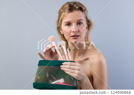 A Young Woman Holding a Transparent Green Cosmetic Bag with Makeup Brushes, Showcasing a Natural Beauty and Emphasizing Minimalistic Skincare and Makeup Essentials A Young Woman Holding a Transparent Green Cosmetic Bag with Makeup Brushes, Showcasing a Natural Beauty and Emphasizing Minimalistic Skincare and Makeup Essentials 124090668