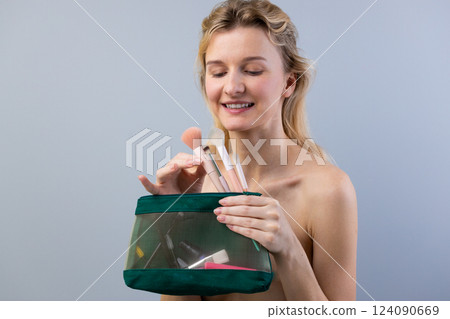 A Cheerful Woman Joyfully Displaying Her Makeup Brushes from a Stylish Transparent Cosmetic Bag Against a Soft Gray Background A Cheerful Woman Joyfully Displaying Her Makeup Brushes from a Stylish Transparent Cosmetic Bag Against a Soft Gray Background 124090669