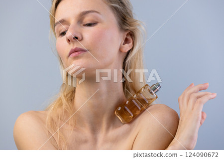 Elegant Woman Showcasing a Perfume Bottle with Graceful Pose and Soft, Natural Makeup Against a Light Gray Background in a Contemporary Fashion Setting 124090672