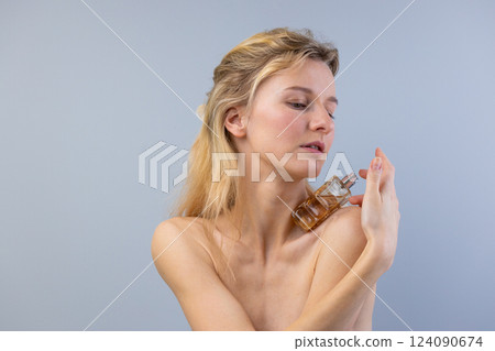 Captivating Moment: A Woman Applying Perfume, Emphasizing Beauty, Elegance, and Self-Care in a Minimalist Setting with Silky Hair and Natural Make-up 124090674