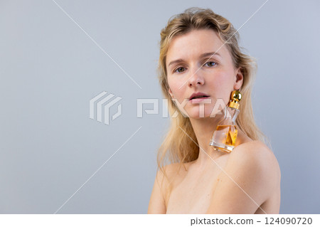 Stunning Artistic Portrait of a Model Featuring a Unique Fashion Element with a Perfume Bottle as an Earring Accessory Against a Minimalist Background 124090720
