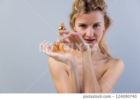 Captivating Female Model Showcasing a Luxurious Perfume Bottle in an Elegant Pose Amidst a Subtle Gray Background 124090740