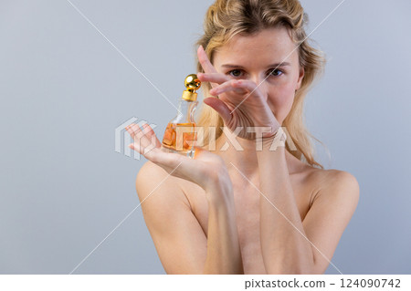 A Captivating Portrait of a Woman Holding a Perfume Bottle, Showcasing Elegance and Charm Against a Soft Gray Background A Captivating Portrait of a Woman Holding a Perfume Bottle, Showcasing Elegance and Charm Against a Soft Gray Background 124090742