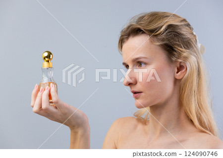 Captivating Portrait of a Woman Holding a Stylish Perfume Bottle, Exuding Elegance and Beauty Against a Soft Grey Background, Ideal for Fashion, Beauty, and Lifestyle Themes Captivating Portrait of a Woman Holding a Stylish Perfume Bottle, Exuding Elegance and Beauty Against a Soft Grey Background, Ideal for Fashion, Beauty, and Lifestyle Themes 124090746