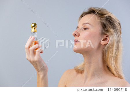 Exploring the Essence of Luxury: A Woman Holding a Beautifully Designed Perfume Bottle with Golden Accents Against a Soft Gray Background Exploring the Essence of Luxury: A Woman Holding a Beautifully Designed Perfume Bottle with Golden Accents Against a Soft Gray Background 124090748