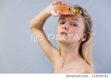 Captivating Encounter with Fragrance: A Model Elegantly Posing with a Classic Perfume Bottle Against a Soft Gray Background, Showcasing Beauty and Sensuality Captivating Encounter with Fragrance: A Model Elegantly Posing with a Classic Perfume Bottle Against a Soft Gray Background, Showcasing Beauty and Sensuality 124090761