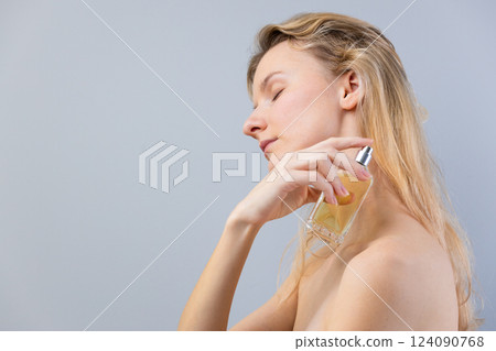 Elegance in Simplicity: Young Woman Applying Perfume with Grace in a Minimalist Setting to Emphasize Personal Care and Beauty Rituals Elegance in Simplicity: Young Woman Applying Perfume with Grace in a Minimalist Setting to Emphasize Personal Care and Beauty Rituals 124090768