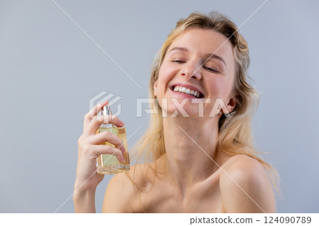Joyful Woman Enjoying Fragrance Application in Front of Gray Background: A Captivating Moment of Self-Care and Scent Exploration 124090789