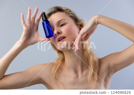 Captivating Beauty: Woman Holding Blue Cosmetic Bottle Close to Her Face for a Serene and Artistic Presentation of Skincare and Self-Care Rituals 124090820