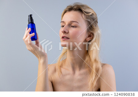 Exploring the Beauty Rituals: A Woman Carefully Examines a Blue Bottled Serum for Skin Care in a Minimalist Setting with Soft Lighting and Natural Elegance 124090838