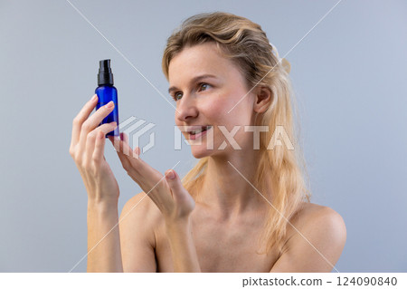 A Woman Observing a Blue Cosmetic Bottle with Enthusiasm, Showcasing the Importance of Skincare in Daily Beauty Routines for Healthy Glowing Skin That Radiates Confidence 124090840