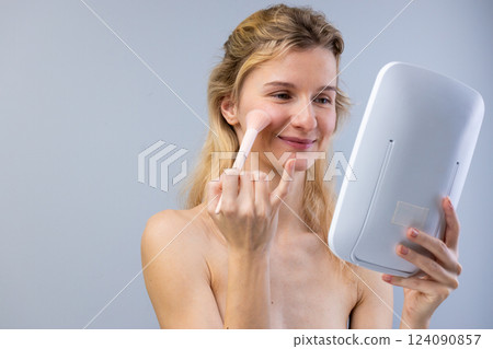 A Woman Applying Makeup in Front of a Mirror: Embracing Natural Beauty with Makeup Techniques and Skincare Choices for a Confident Appearance A Woman Applying Makeup in Front of a Mirror: Embracing Natural Beauty with Makeup Techniques and Skincare Choices for a Confident Appearance 124090857