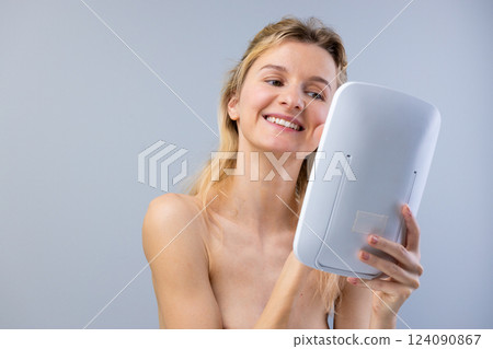 A Young Woman Smiling at Her Reflection in the Mirror, Emphasizing Self-Care and Beauty Routine with Natural Radiance and Positivity in a Minimalistic Environment A Young Woman Smiling at Her Reflection in the Mirror, Emphasizing Self-Care and Beauty Routine with Natural Radiance and Positivity in a Minimalistic Environment 124090867
