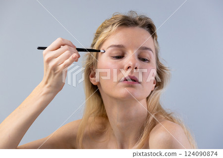 A young woman engaged in a beauty routine, applying makeup with a brush, emphasizing her concentration, showcasing a commitment to self-care and aesthetic enhancement. 124090874