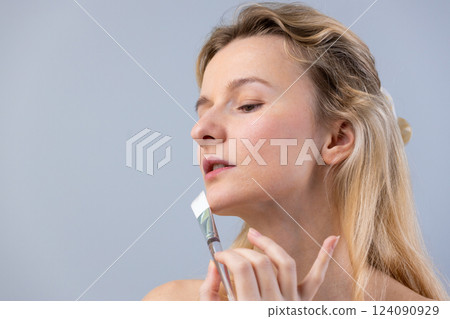 A Young Woman Applying Skincare Cream on Her Face with a Brush in a Calm and Relaxed Manner, Highlighting Beauty and Self-Care Routines for a Radiant Complexion A Young Woman Applying Skincare Cream on Her Face with a Brush in a Calm and Relaxed Manner, Highlighting Beauty and Self-Care Routines for a Radiant Complexion 124090929