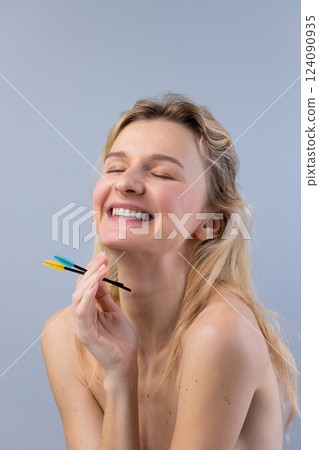 A Joyful Moment of Self-Care: A Woman Expressing Happiness While Holding Cosmetic Tools for Eyebrow Grooming in Front of a Soft Gray Background A Joyful Moment of Self-Care: A Woman Expressing Happiness While Holding Cosmetic Tools for Eyebrow Grooming in Front of a Soft Gray Background 124090935