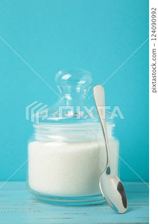 Jar with white sugar on blue background. Vertical photo 124090992