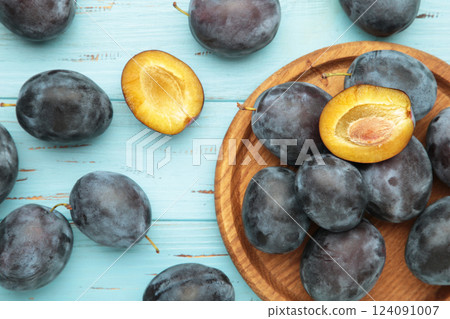 Fresh plums on wooden plate on blue wooden background 124091007