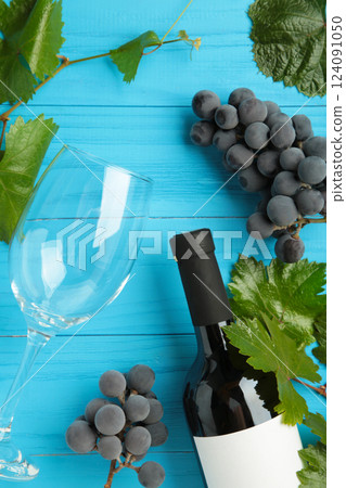 Wine bottle and wine glass with grapes on blue wooden background. Vertical photo 124091050