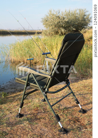 Fisherman's chair and fishing rods in the background over the river at sunrise, foggy morning. Fishing concept. Vertical photo 124091069
