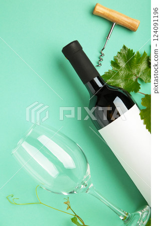 Wine bottle with wine glass and corkscrew lying on mint background. Vertical photo 124091196