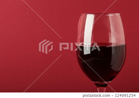 Dark studio shot of glass of red wine on dark red background. Space for text 124091254