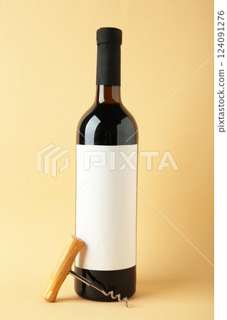 Bottle with red wine and corkscrew on beige background. Vertical photo 124091276
